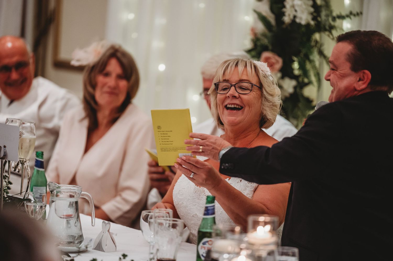 People enjoying drinks and laughter at a formal dinner table with white tablecloth and glassware.