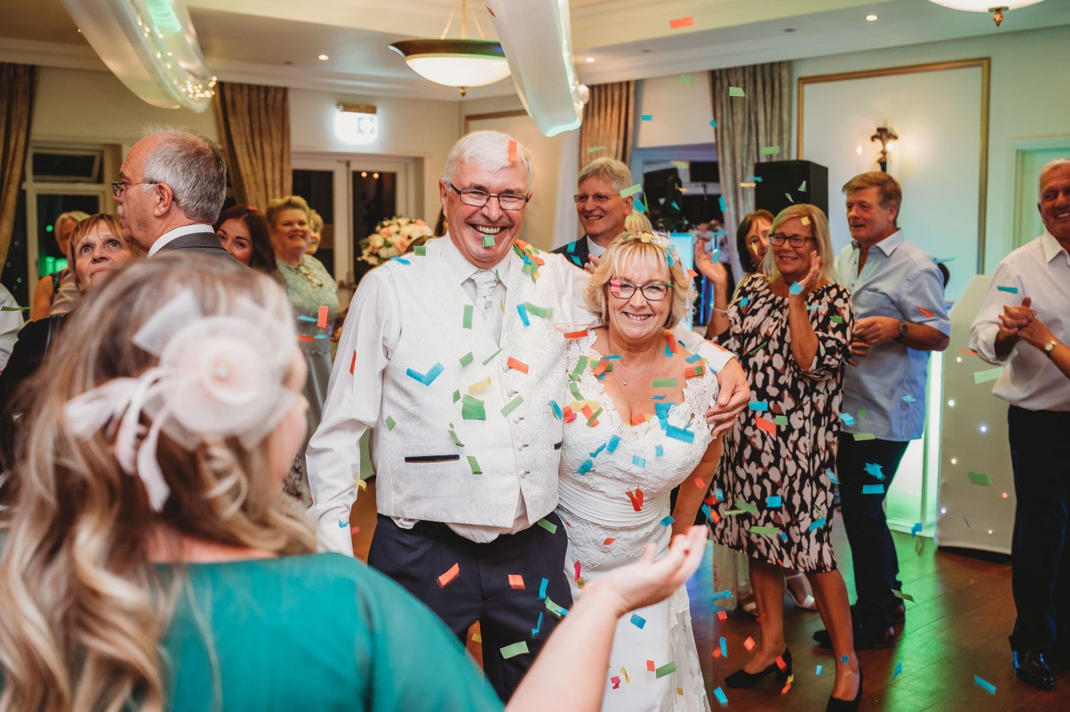Wedding celebration with guests enjoying confetti falling during a joyful moment on the dance floor at an indoor reception.