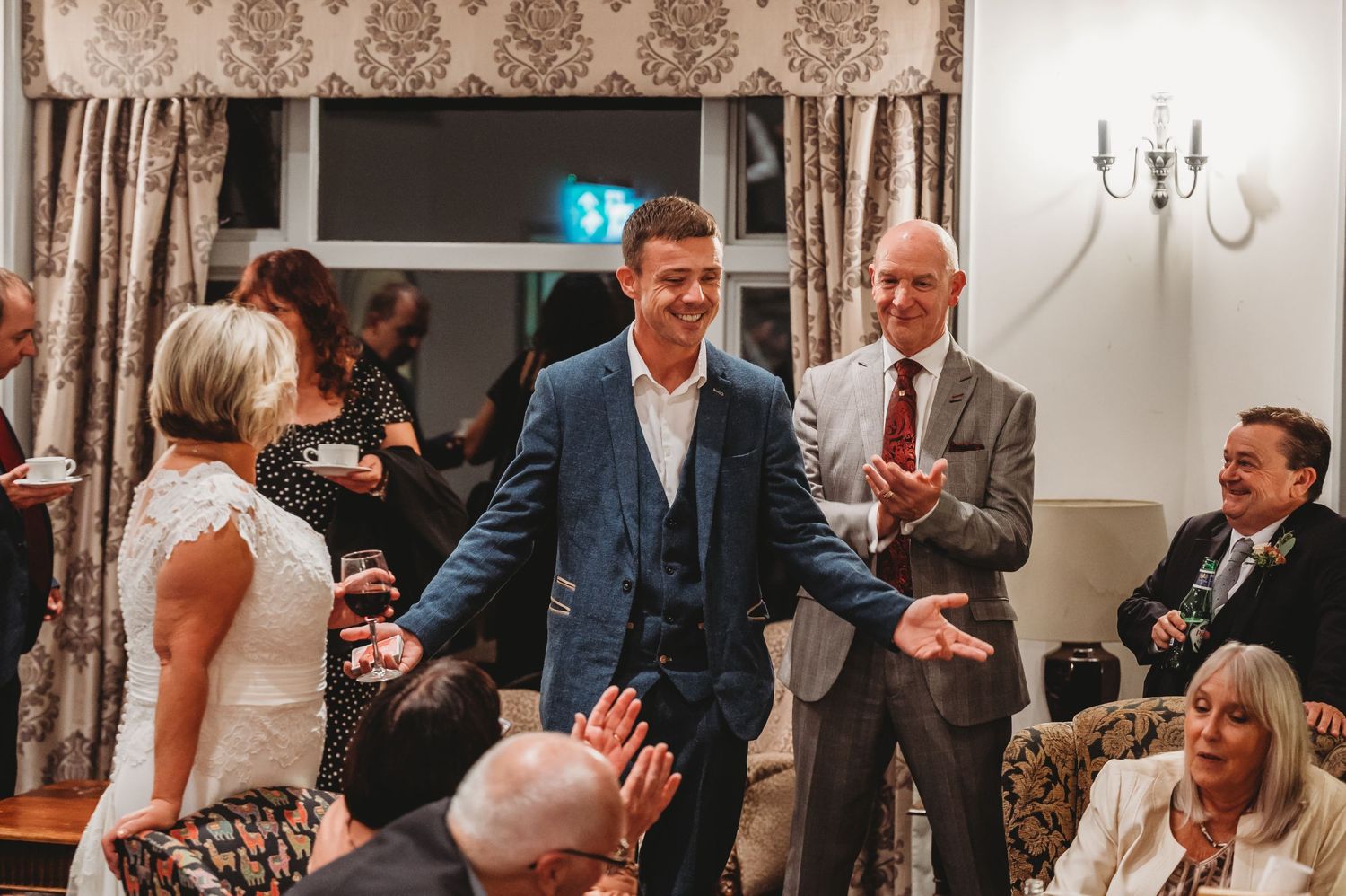 A lively moment at an elegant wedding reception with guests mingling and laughing in a formal room with vintage decor.