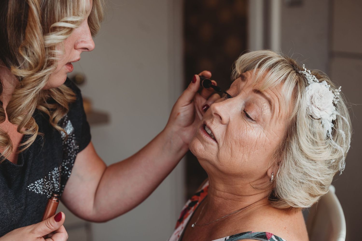Makeup artist applies delicate eye cosmetics on bride wearing pearl hairpiece during wedding preparation.