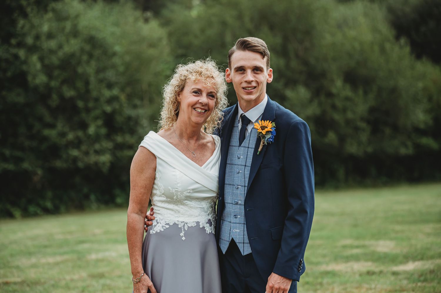 A joyful couple poses outdoors on their wedding day, with green foliage in the background.