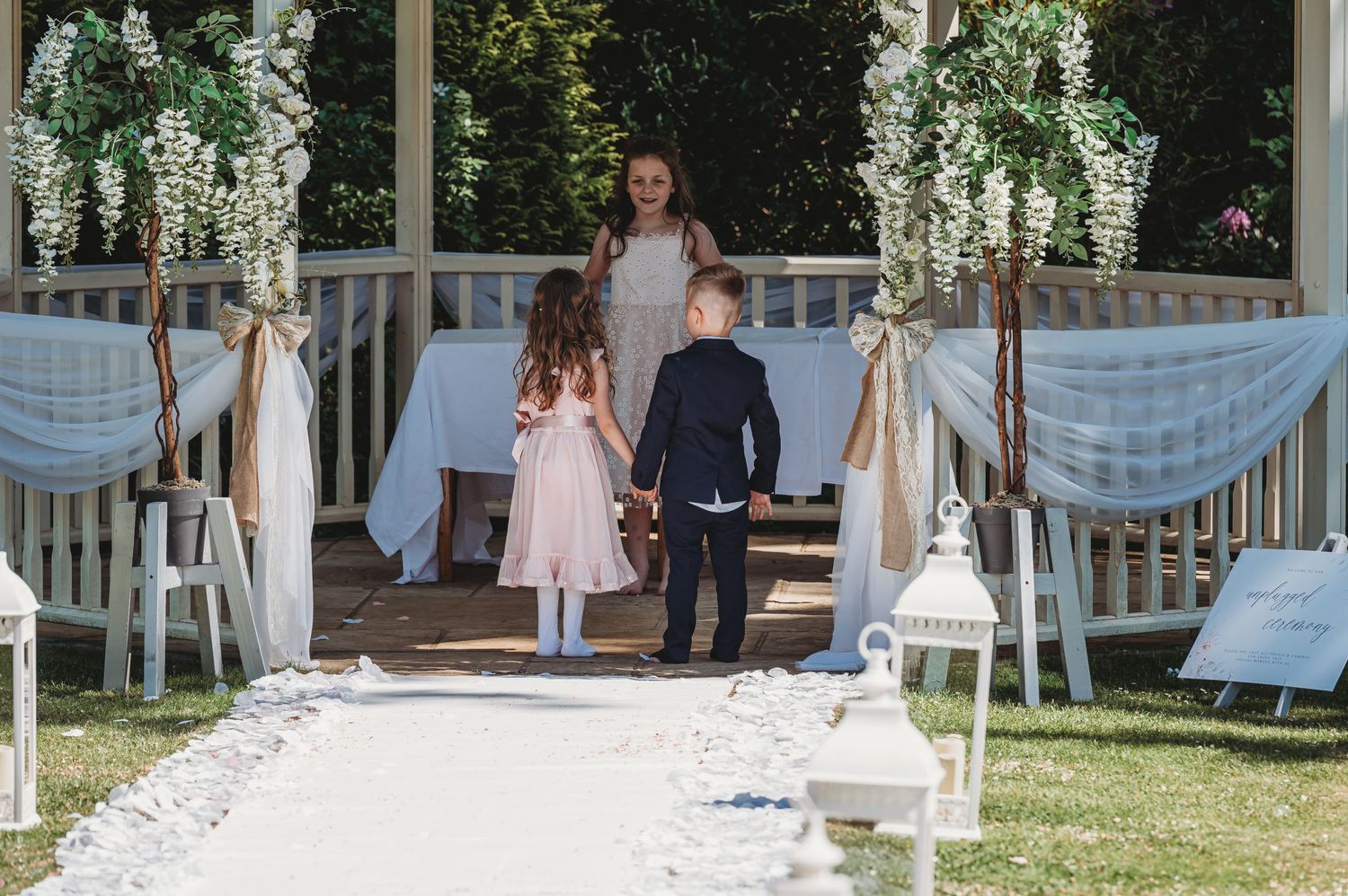 An outdoor wedding ceremony setup with white draped decor, floral arrangements, and a stone pathway leading to the altar.