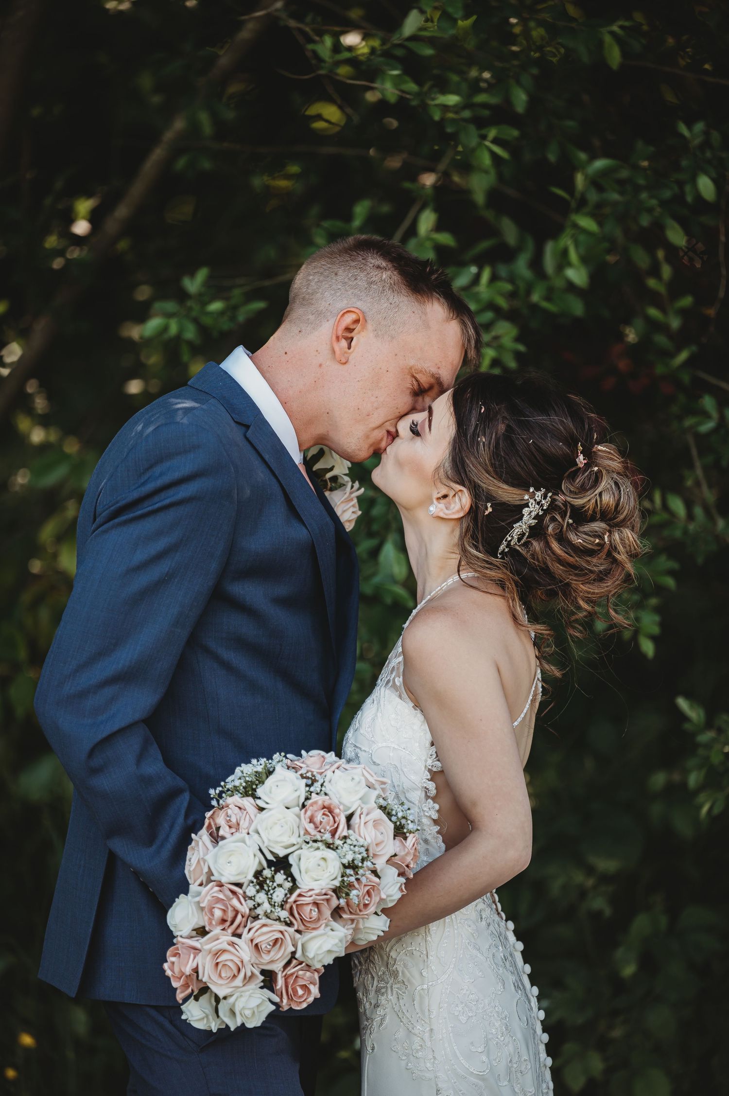 A romantic wedding moment captured outdoors with blush pink rose bouquet against lush greenery background.