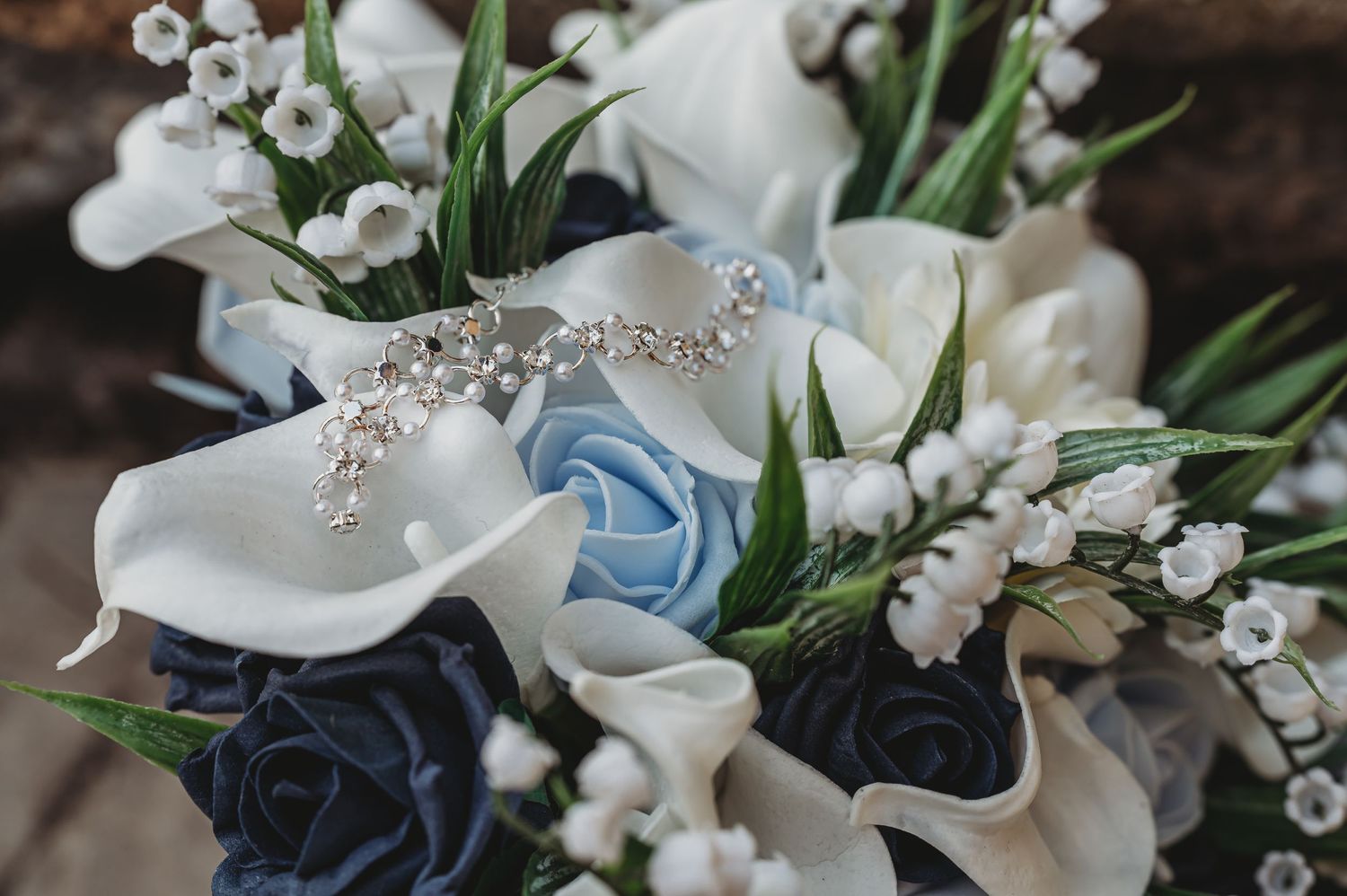 Elegant wedding bouquet with white calla lilies, light blue roses, and delicate sparkly accents against a dark background.