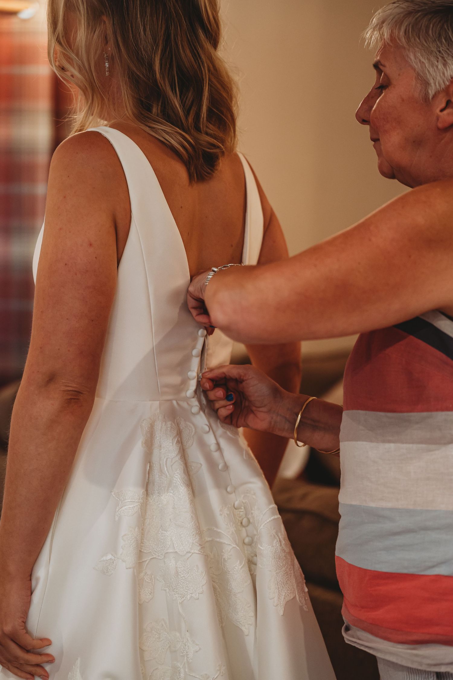 Someone helps with the final adjustments of a white wedding dress during pre-ceremony preparations.