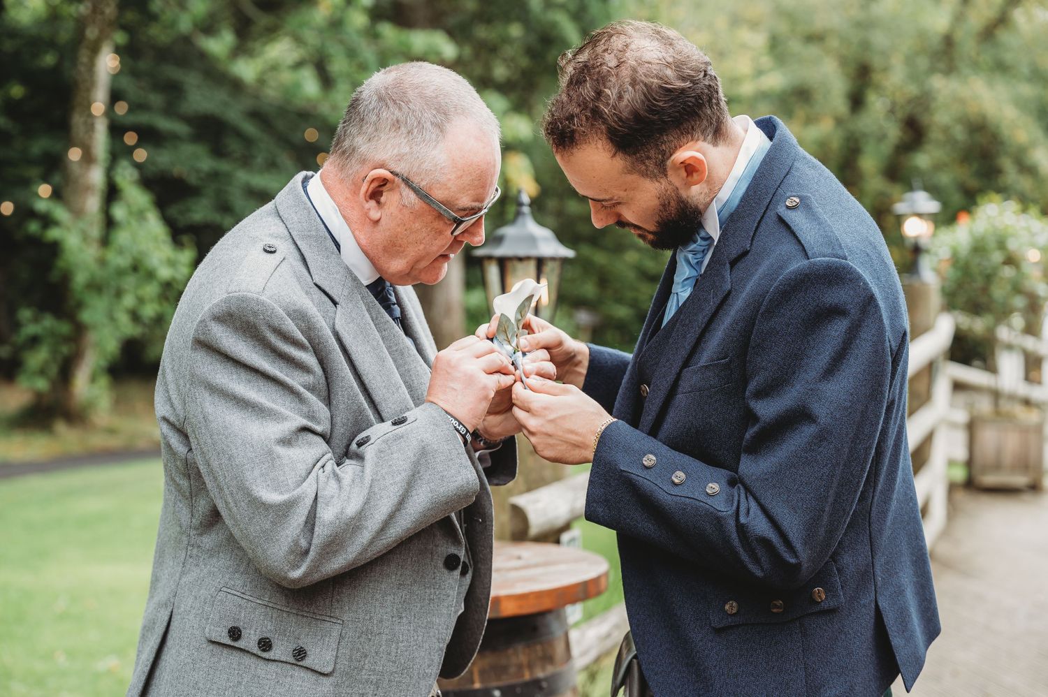 Two men in suits examining something closely while standing together in a garden path.
