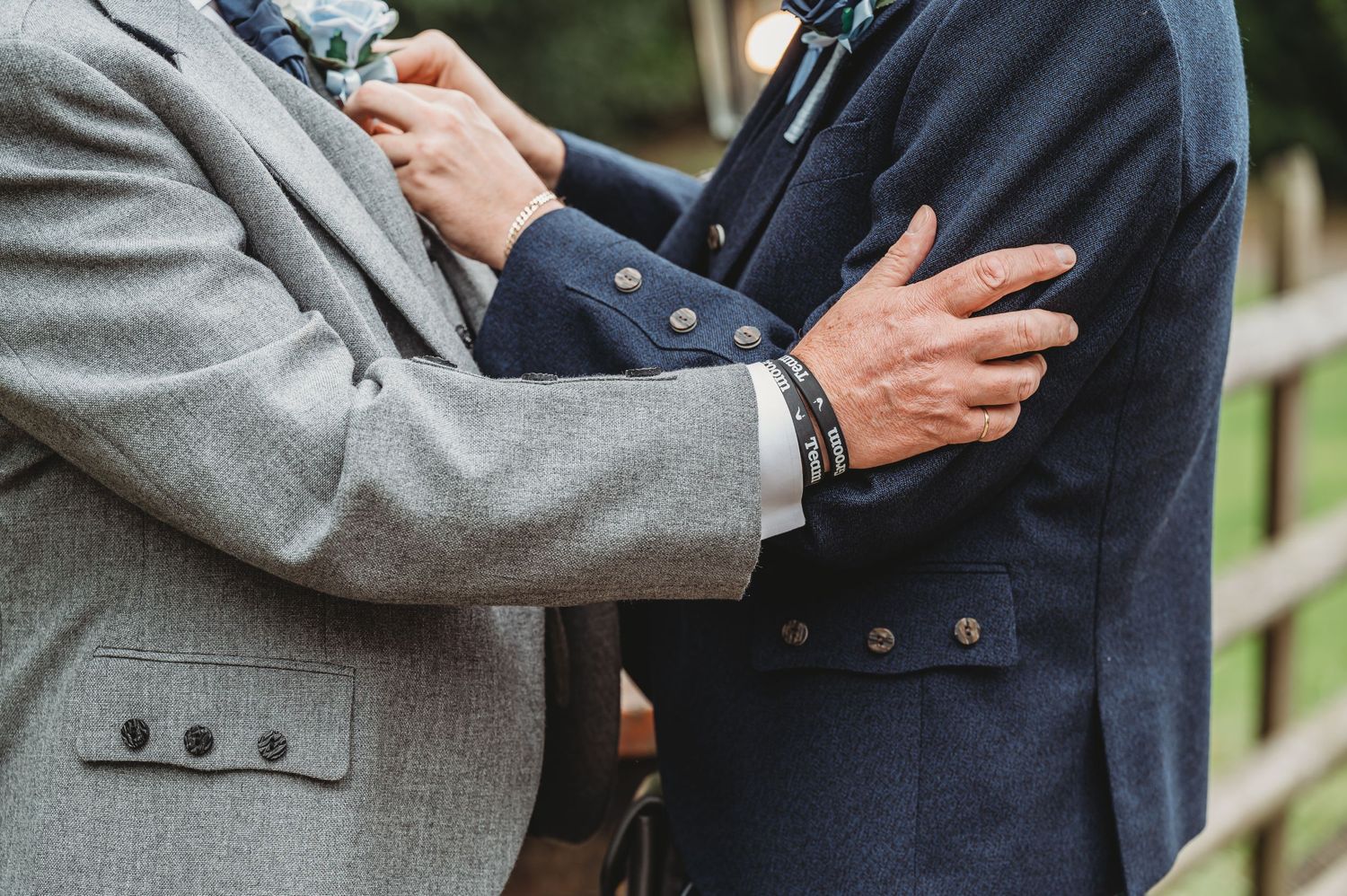 Two people in formal attire embrace, showing close up detail of suit jackets in navy and gray.