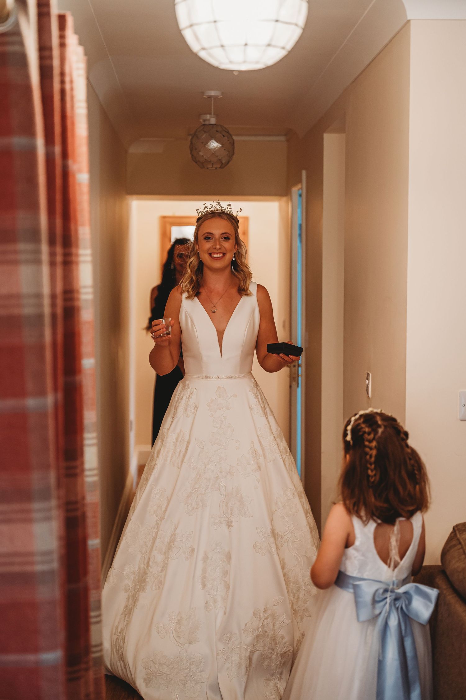 Beautiful bride in white plunging v-neck ballgown walks down hallway with flower girl in white dress with blue bow.
