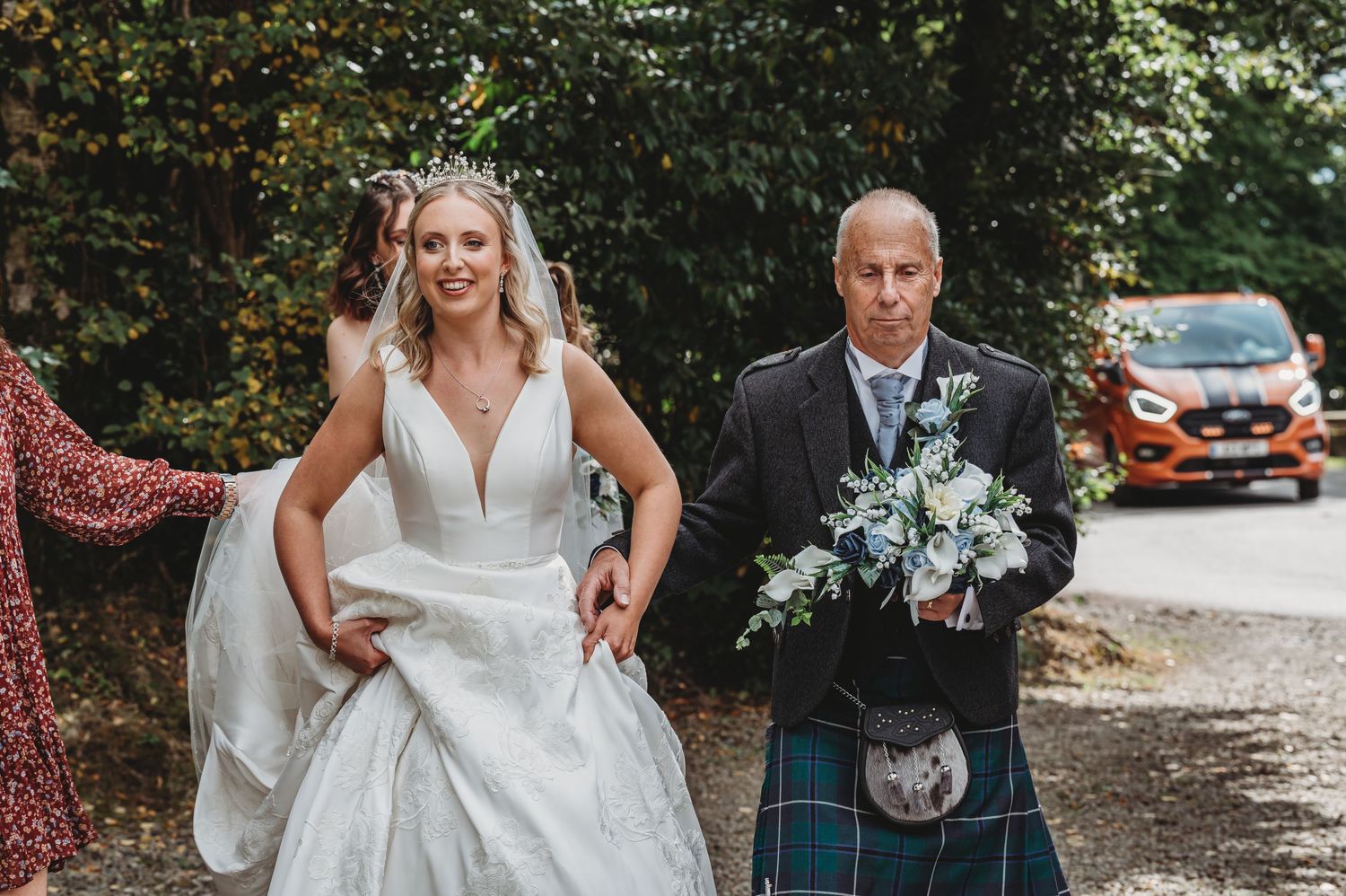 A couple walking together on a path, with the person on the left wearing a white wedding dress and the right in a kilt.