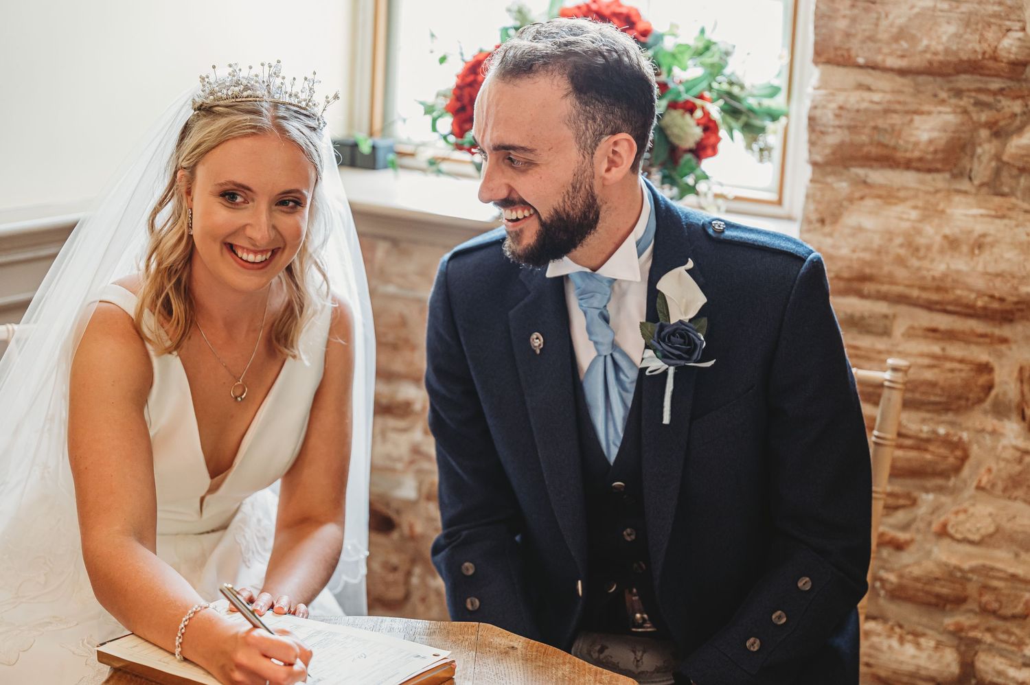 Bride and groom share a laughing moment during wedding ceremony signing at rustic stone venue.