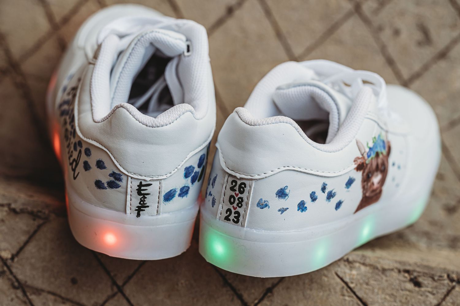 White light-up sneakers with blue floral details and LED lights glowing in orange and green colors.