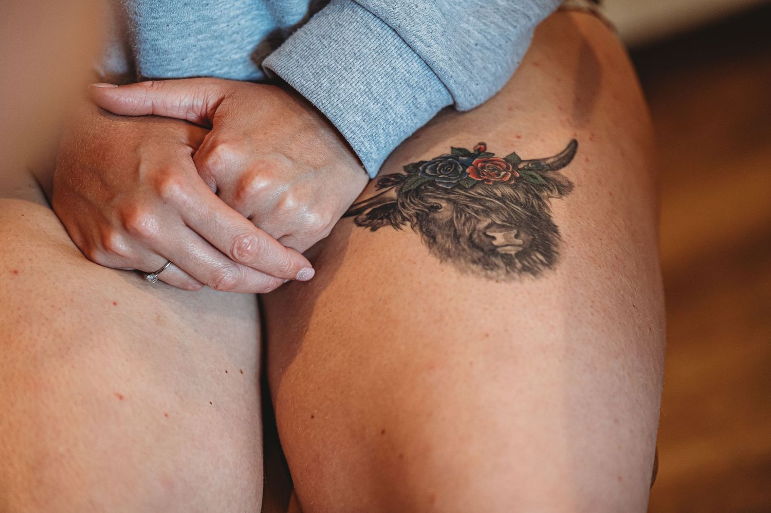 Close-up of a feather tattoo design on bare skin with hands resting nearby.
