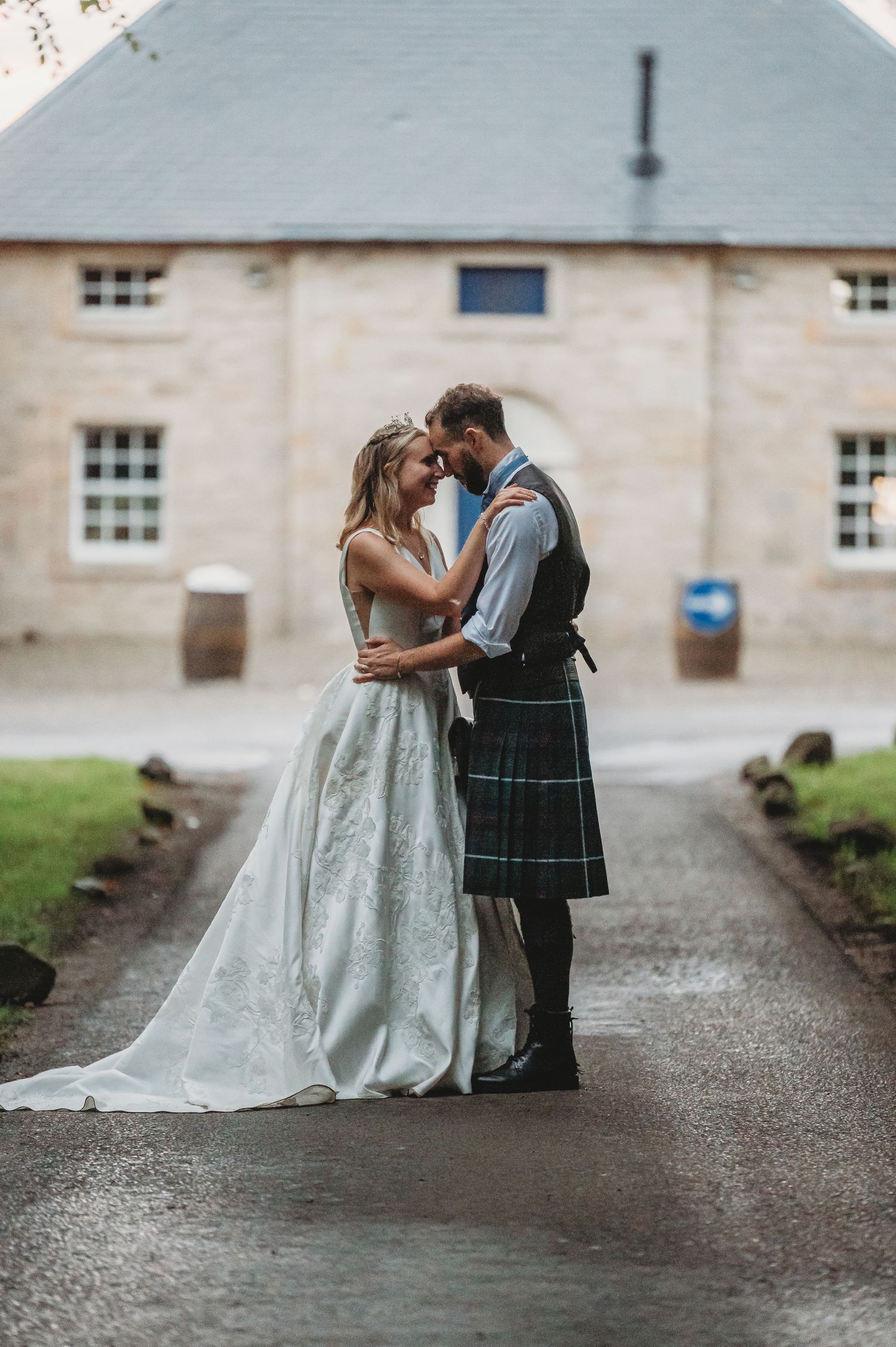 A romantic wedding moment outside a Scottish manor with the bride in white and groom in traditional Highland dress.