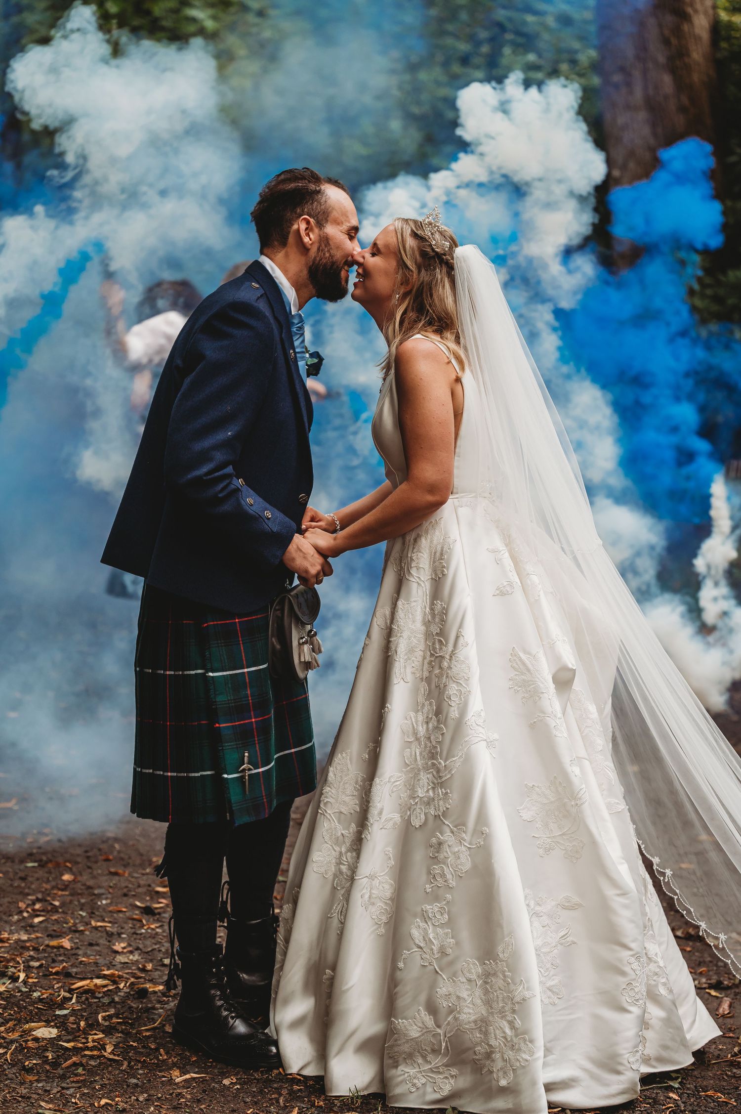 A romantic wedding photo with colorful blue smoke bombs creating a dramatic backdrop while the couple shares a moment.