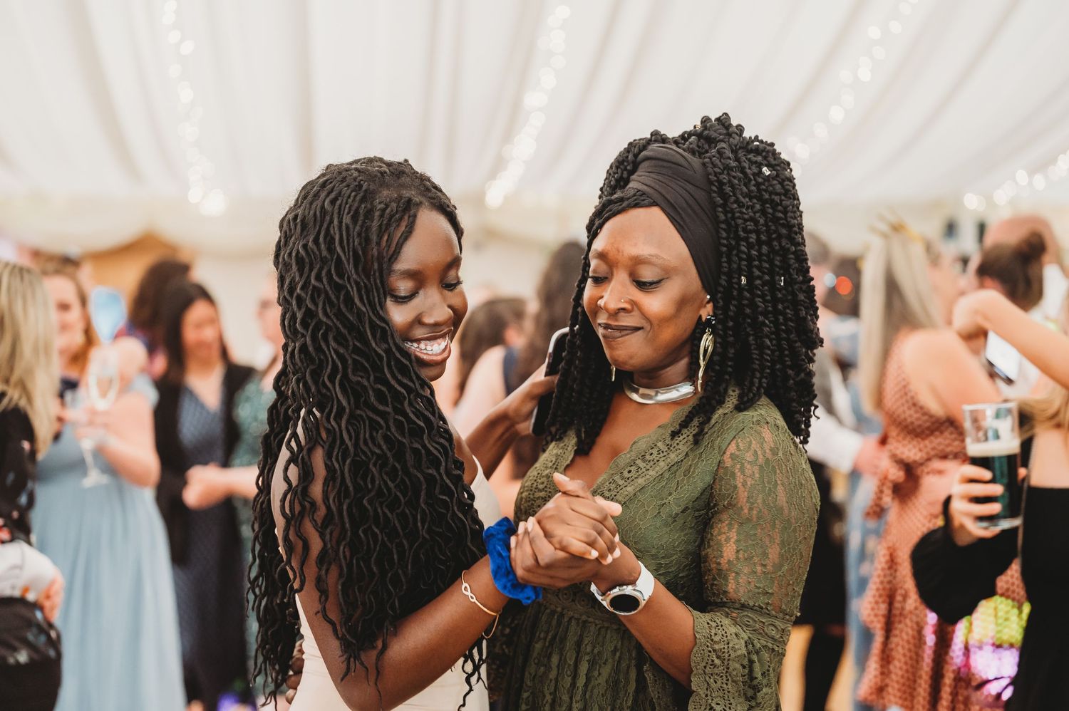 Two guests with braided hair share a joyful dance together at a wedding reception under a white tent.
