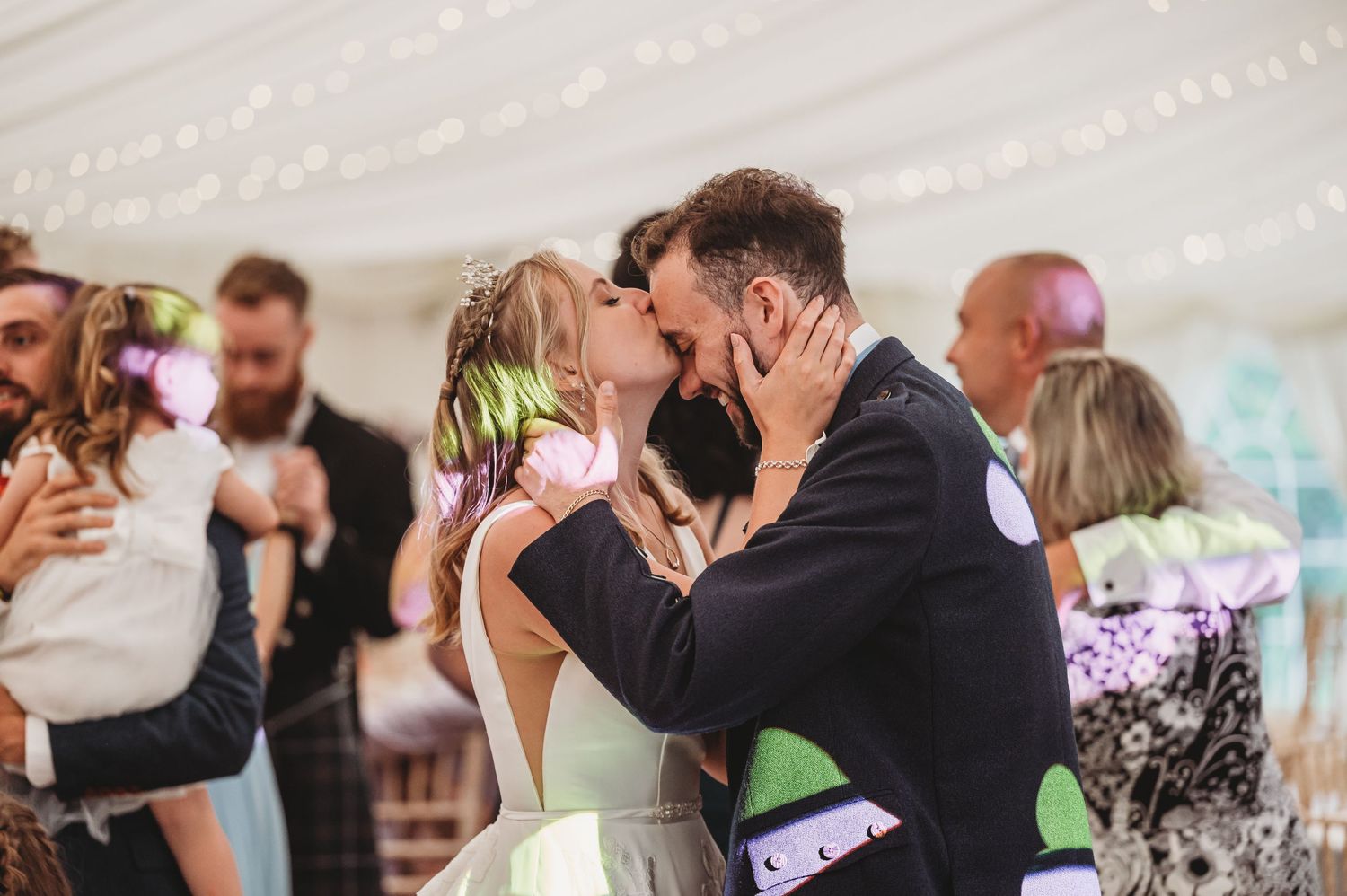 A couple shares their first kiss as newlyweds during a romantic celebration in a tent reception venue.