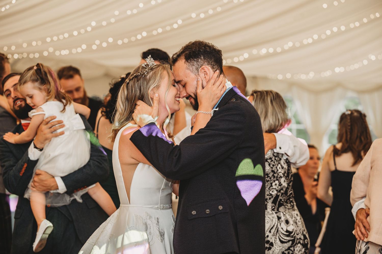 Couple shares an intimate dance moment under twinkling lights during wedding reception in a tent.