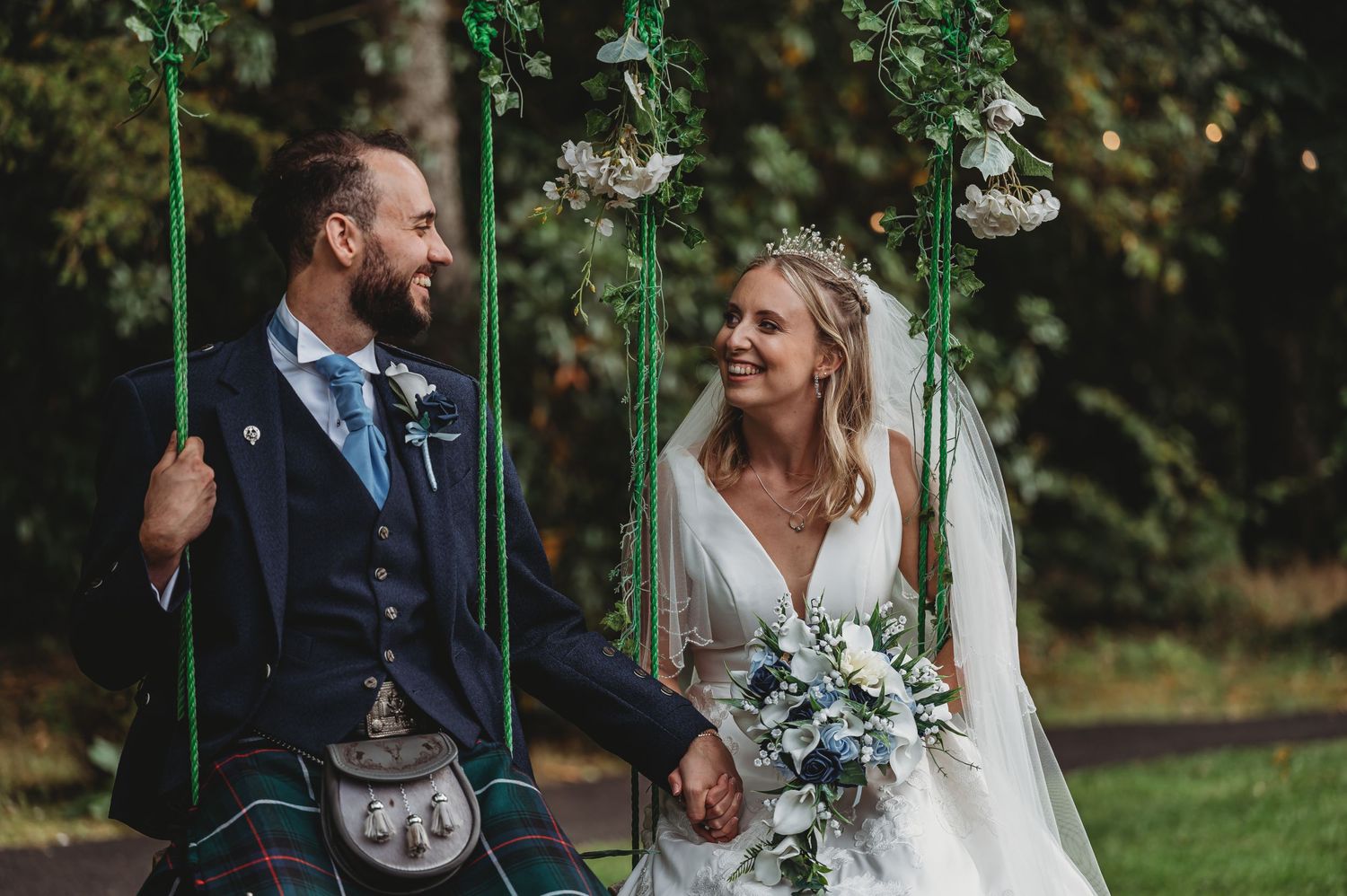 A happy couple in wedding attire share a candid moment while sitting together on garden swings.