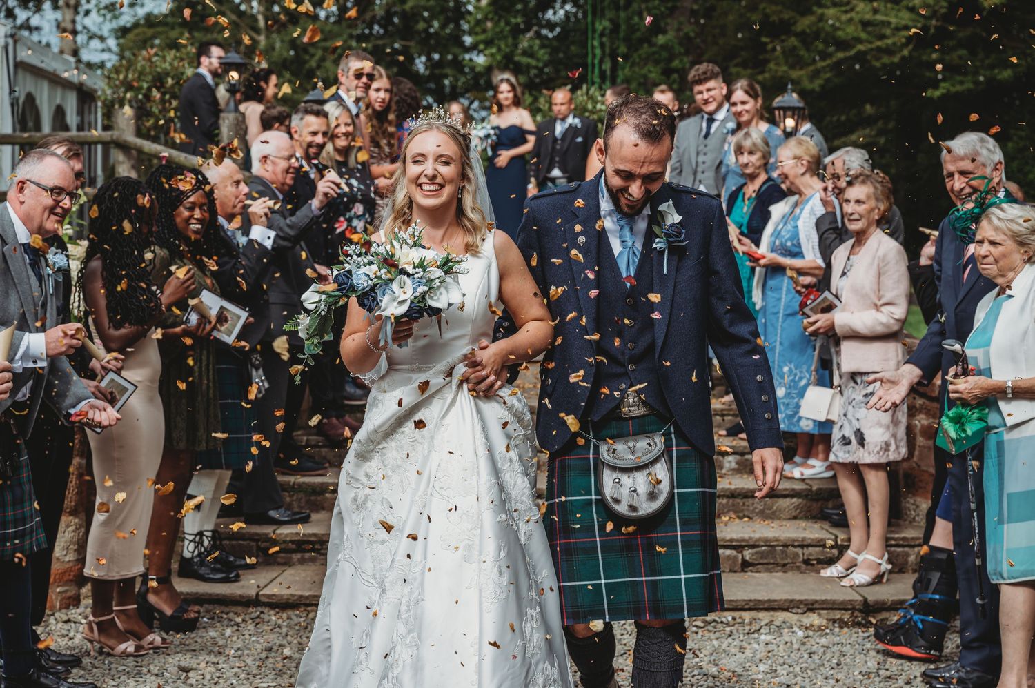 Newlyweds showered with confetti walk down stone steps at an outdoor Scottish wedding ceremony.
