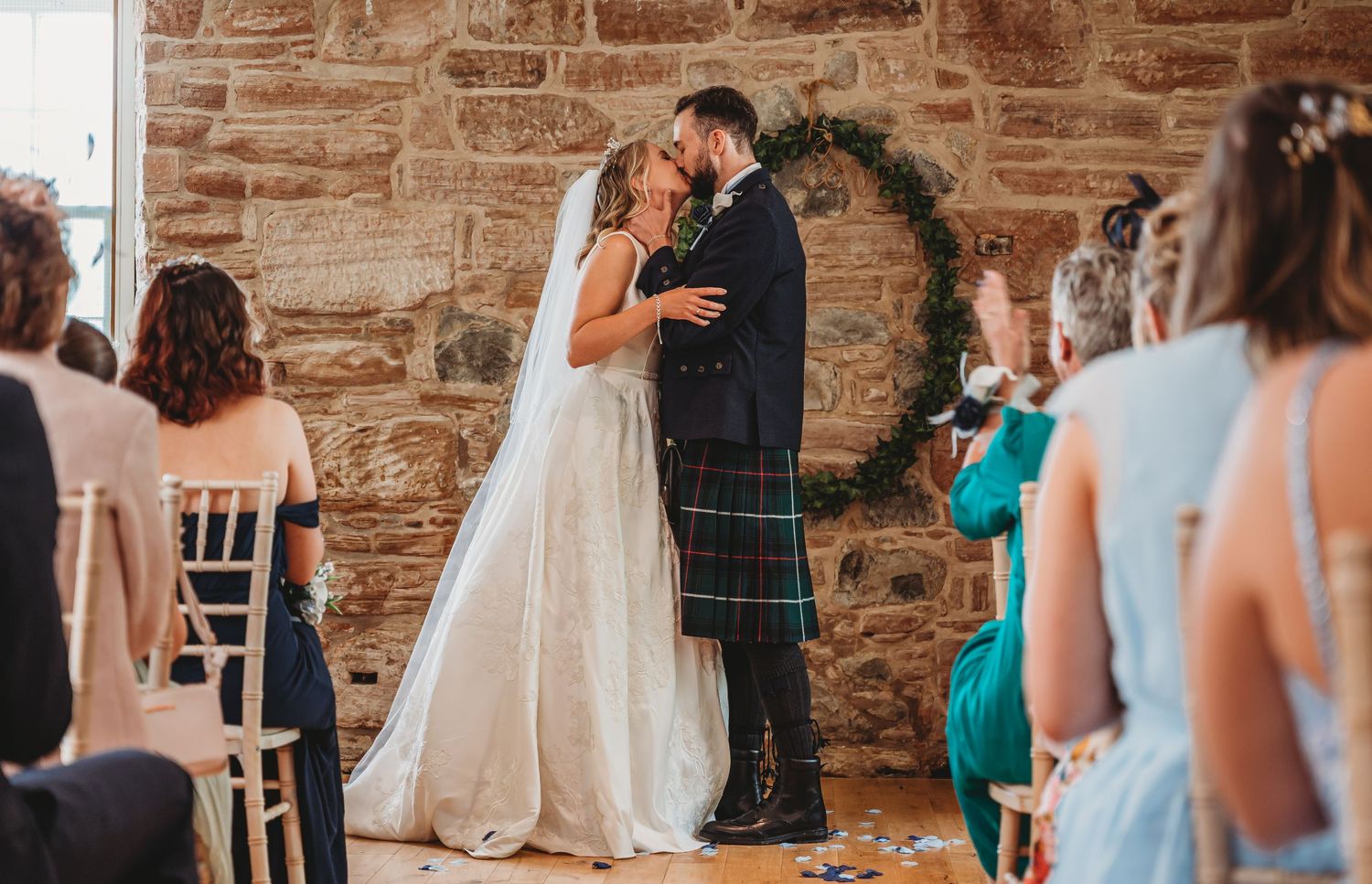 A couple shares their first dance at a rustic stone venue surrounded by seated wedding guests.