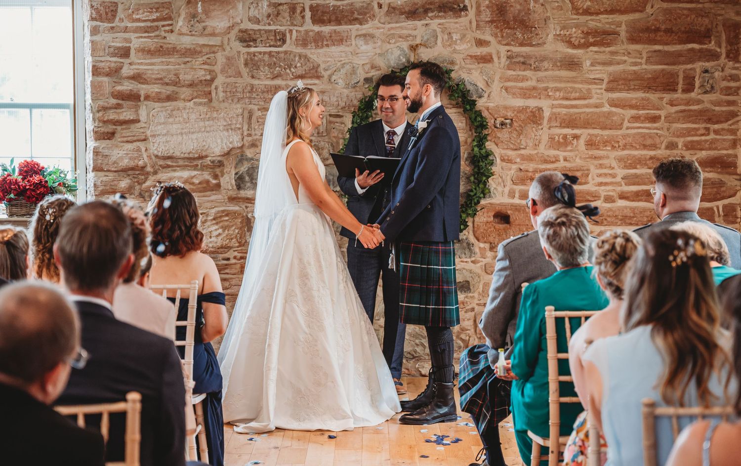 Beautiful wedding ceremony in rustic brick venue with traditional Scottish kilt and flowing white gown.