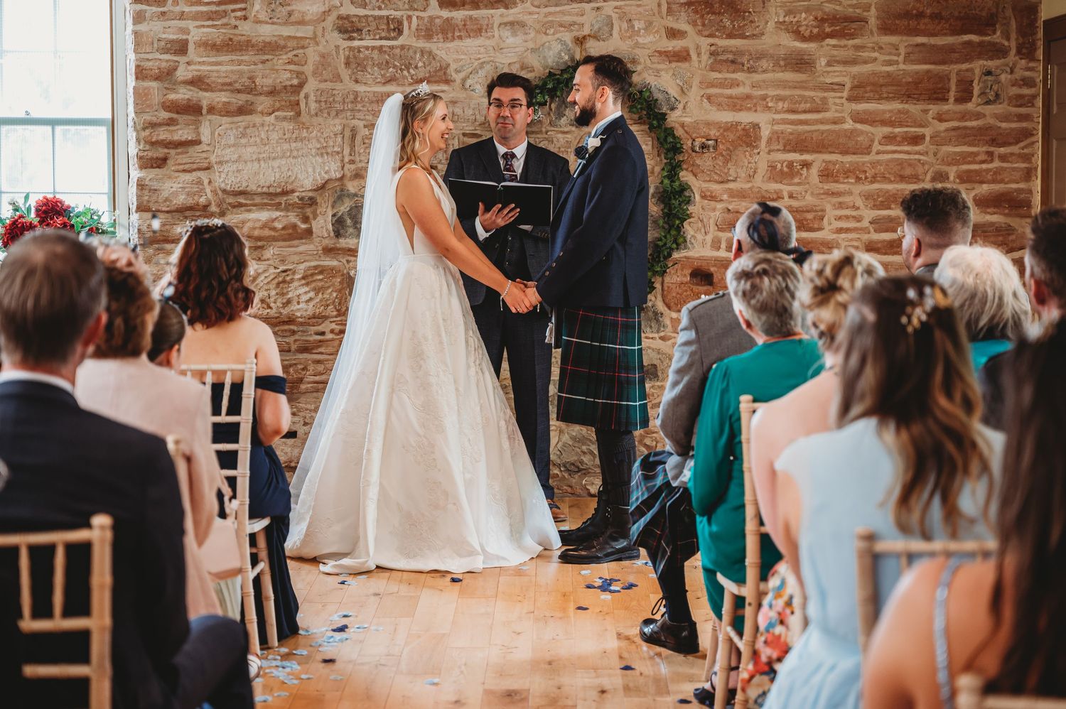 Wedding ceremony takes place inside rustic brick venue with guests seated in chairs watching couple exchange vows.