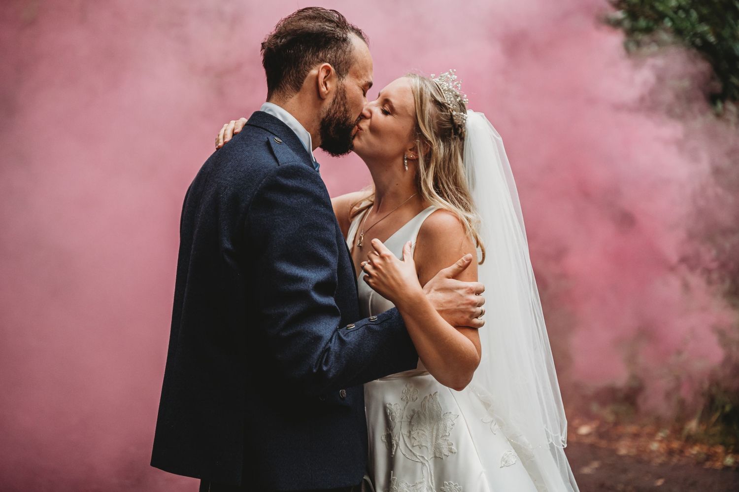 A romantic wedding couple embraces in front of pink smoke during an outdoor photo session.