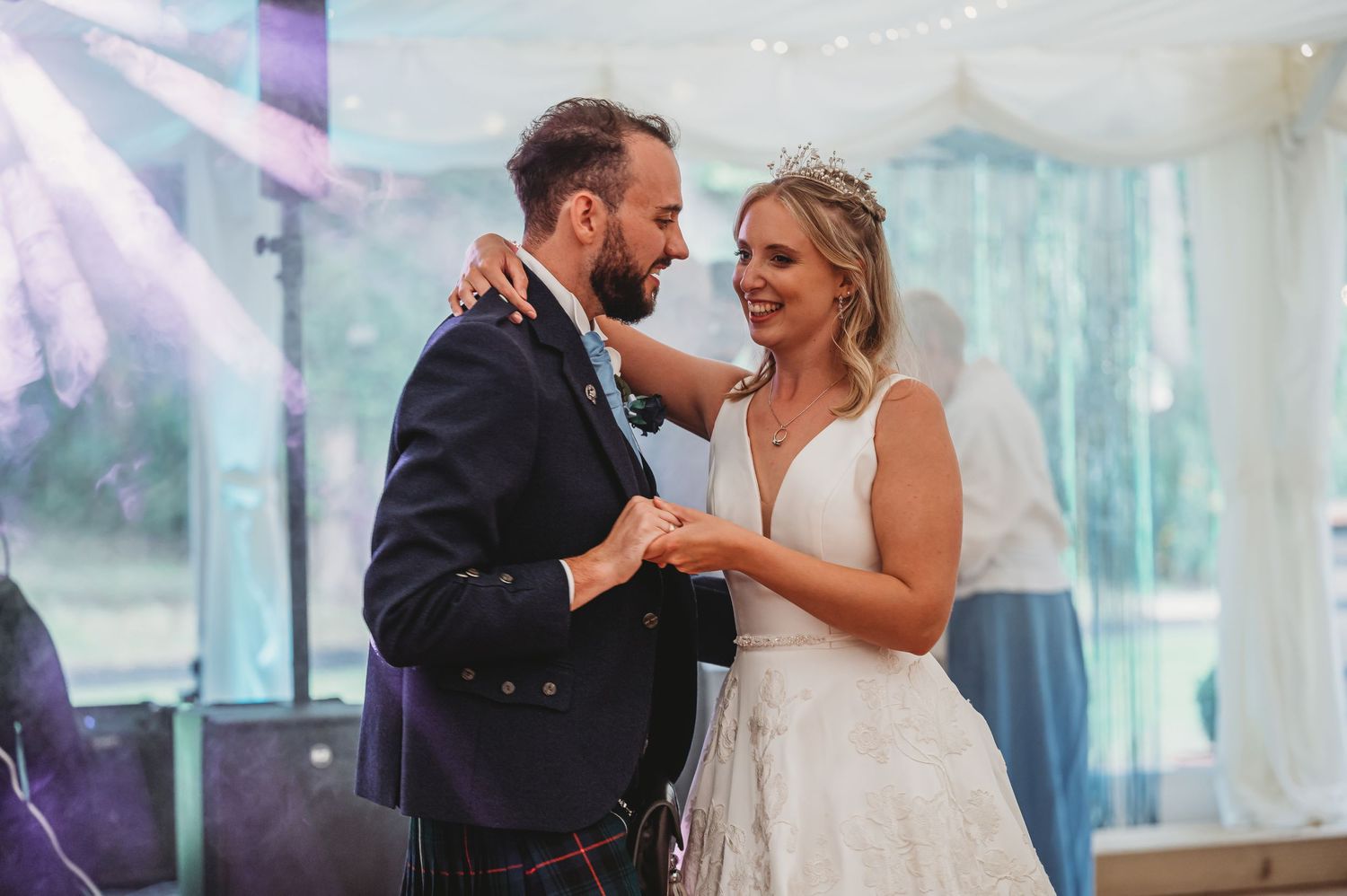 A newlywed couple shares their first dance together at a wedding reception under soft purple lighting.