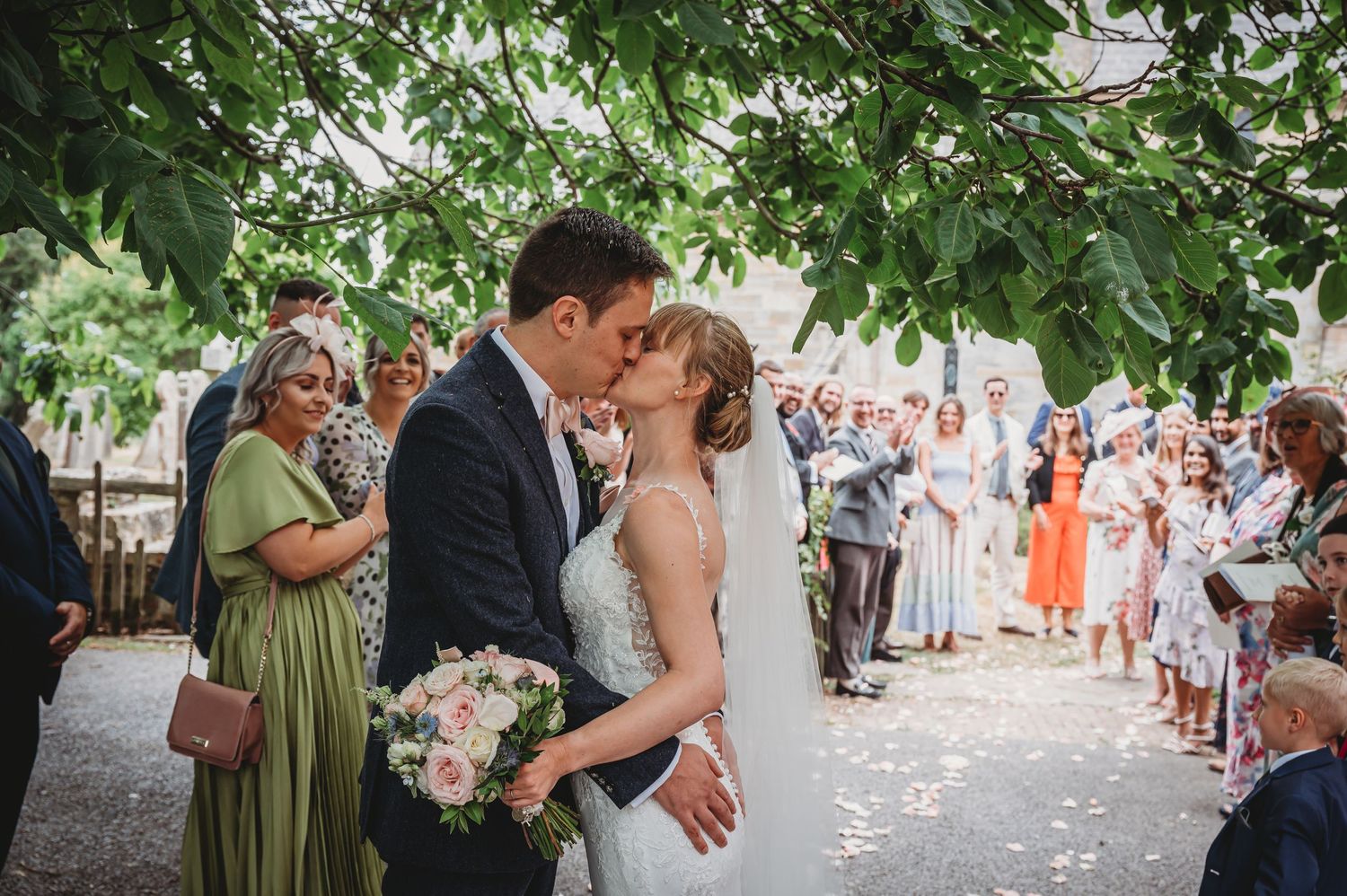 A newlywed couple shares a romantic kiss during their outdoor garden wedding ceremony as guests look on.