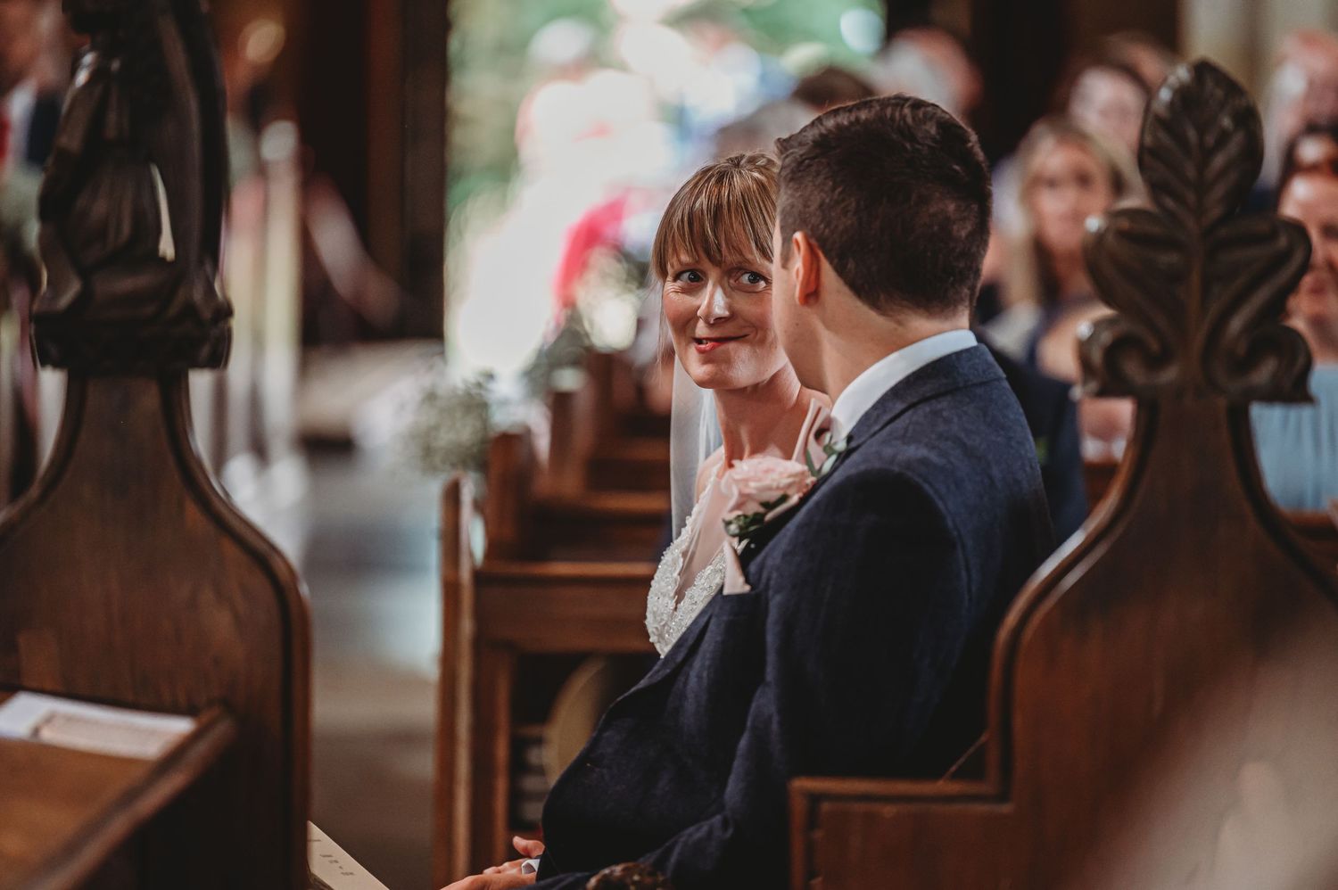 Couple sitting together on wooden church pews in an intimate moment during wedding ceremony.