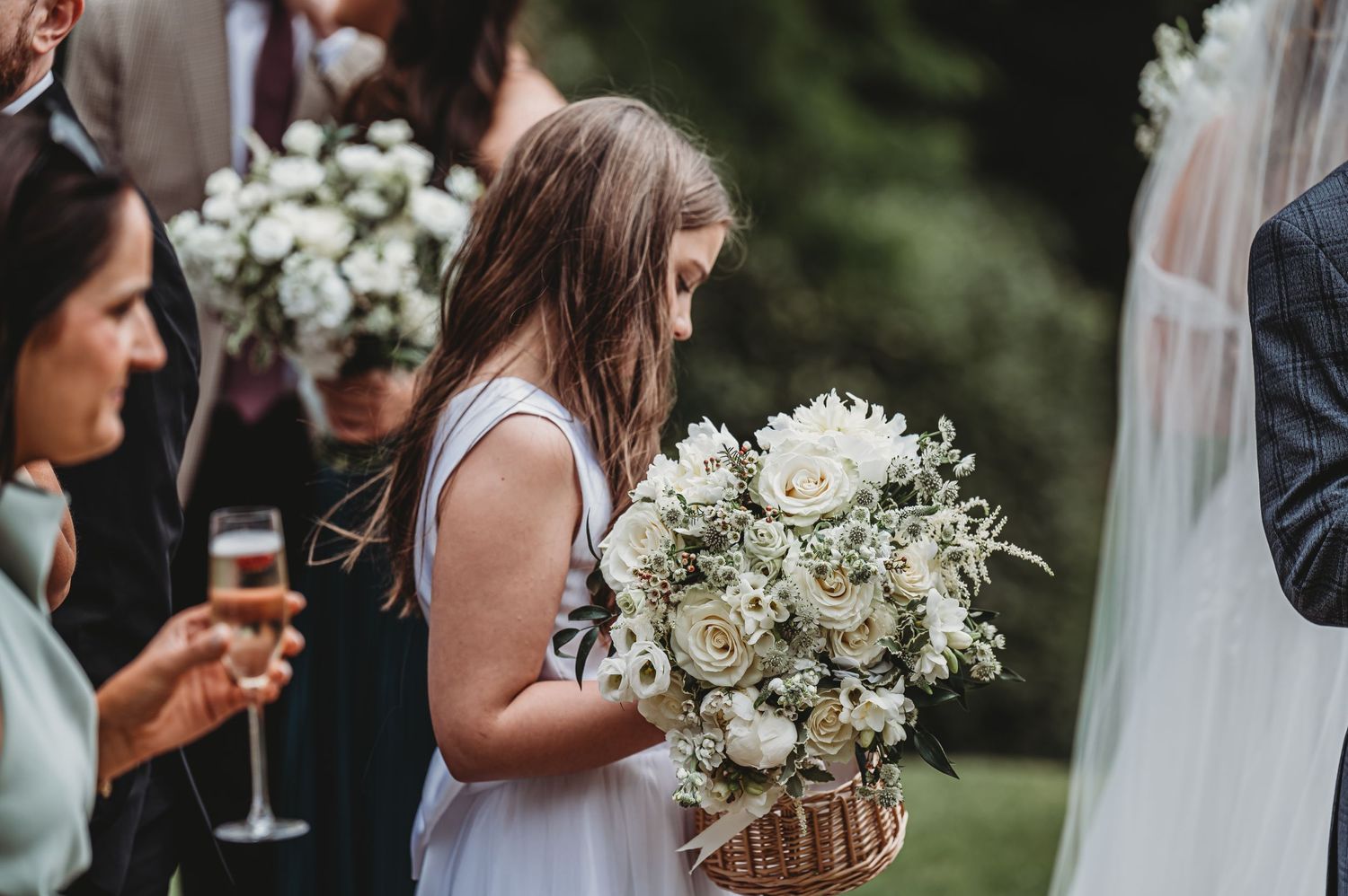 Guest holding elegant white floral bouquet during outdoor wedding reception.