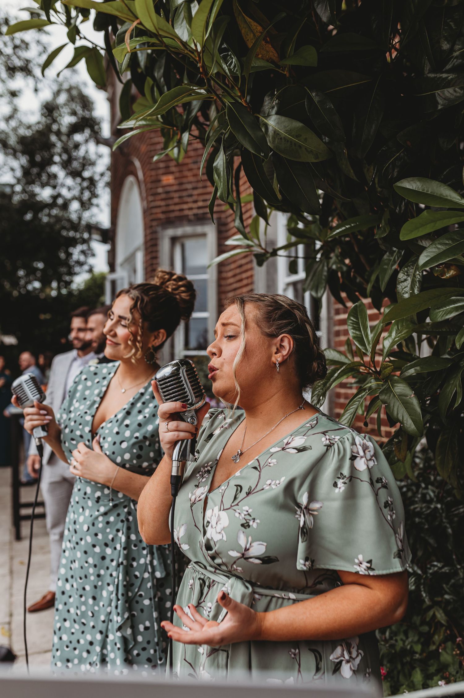 Wedding guests in sage green dresses enjoy drinks during outdoor celebration.