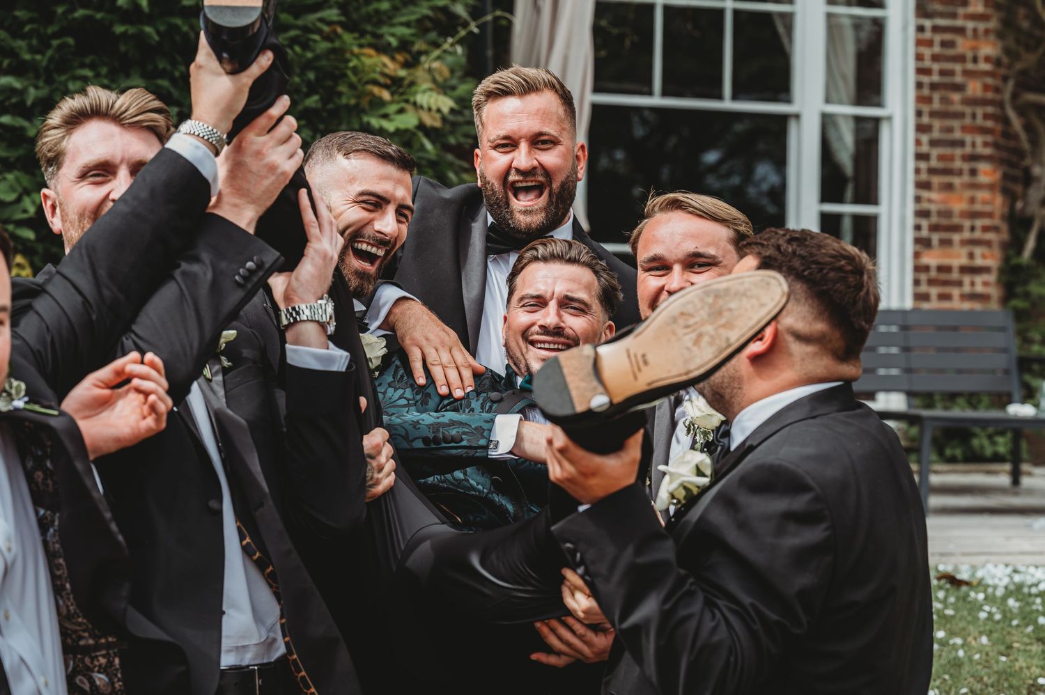 Groomsmen celebrate with drinks and laughter during outdoor wedding festivities.