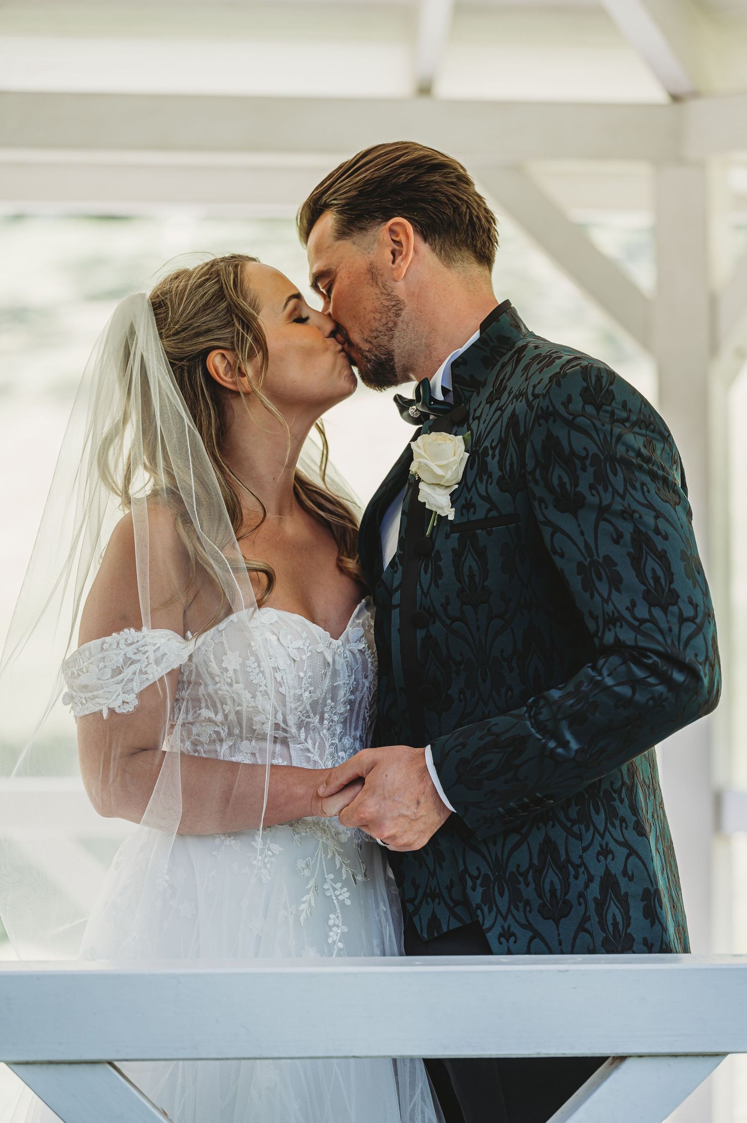 A romantic wedding moment captured with the bride in white lace and groom in dark patterned suit sharing a tender kiss.