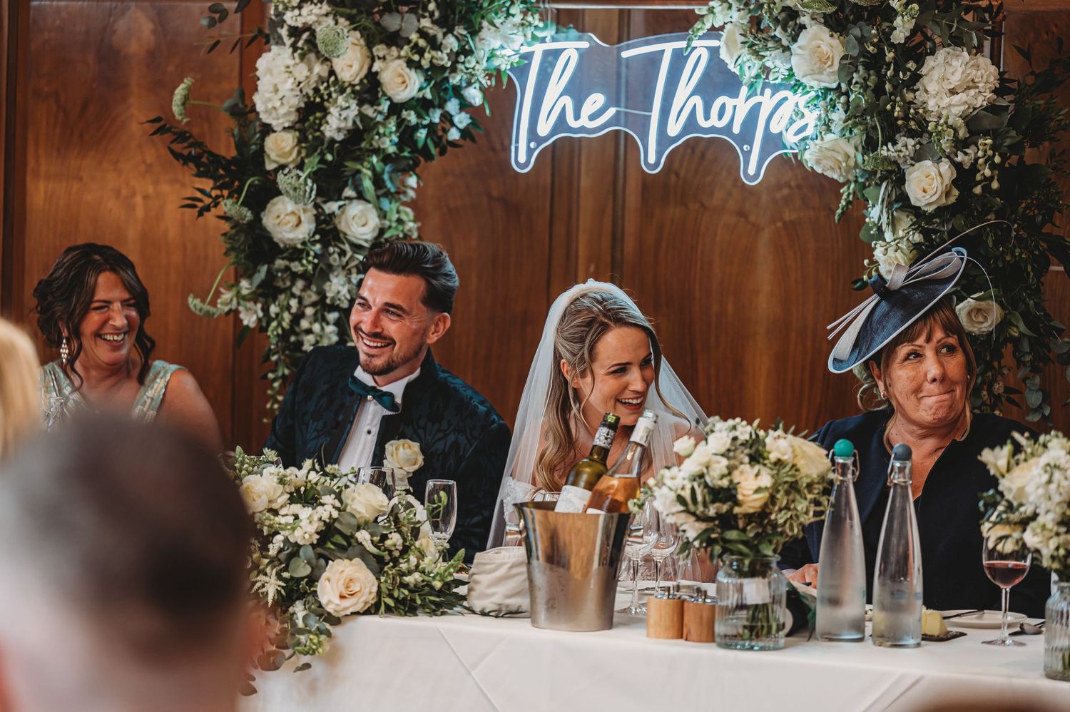 Wedding reception table decorated with floral arrangements and neon signage.