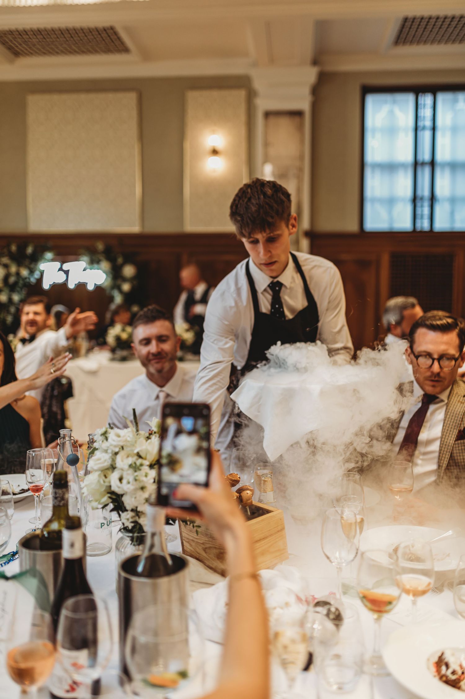 Server presents a dramatic dish with smoke effects at an elegant wedding reception.