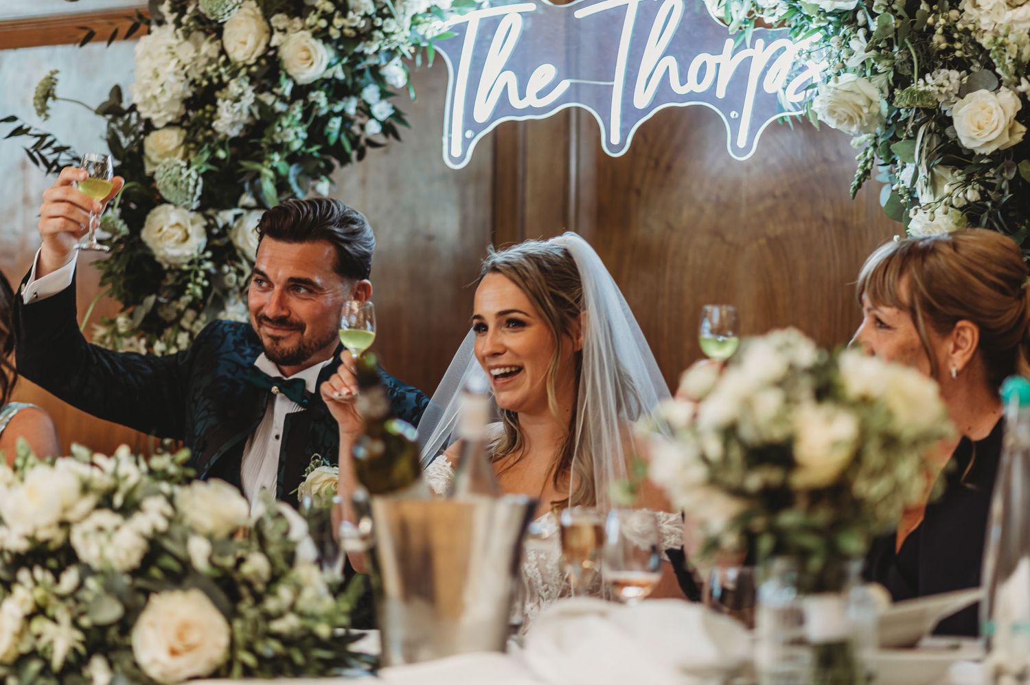Wedding guests celebrate at an elegantly decorated reception with floral arrangements and neon signage.