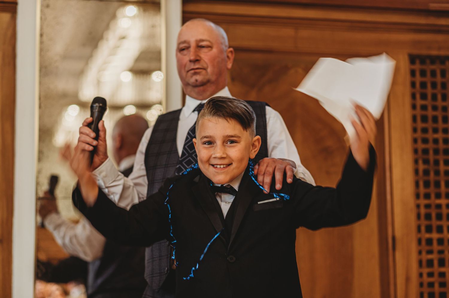 A young boy in formal attire celebrates enthusiastically during wedding speeches.