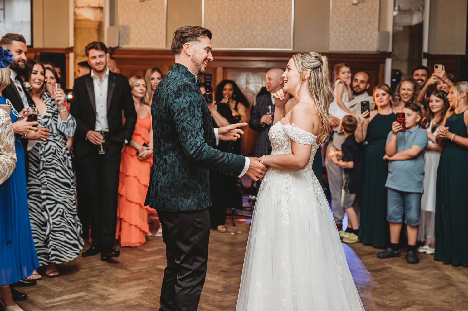 Newlyweds dance together while guests in colorful attire look on and celebrate.
