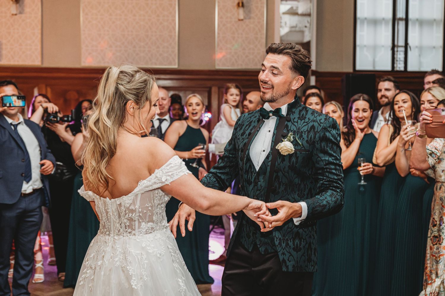 Wedding couple performs their first dance with guests watching in formal attire.