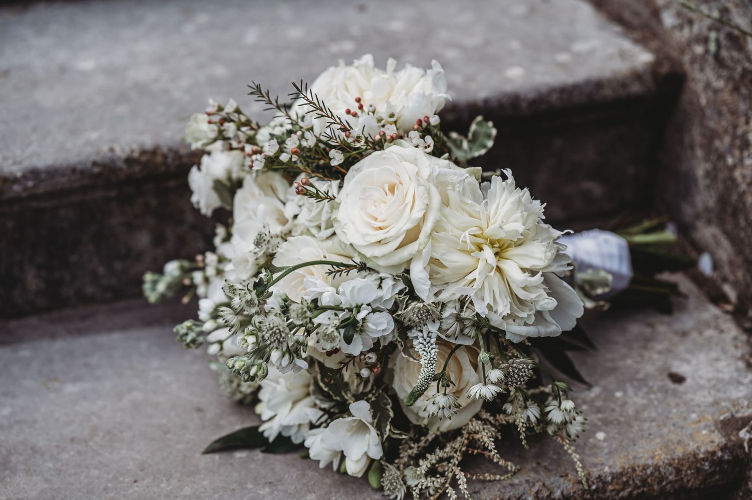 Elegant white wedding bouquet with roses and delicate baby's breath lying on concrete steps.