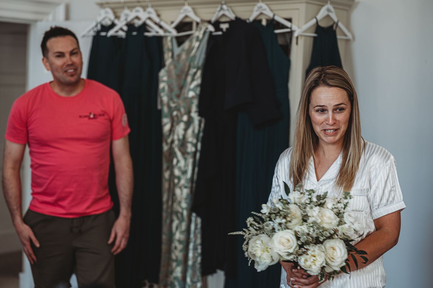 Wedding preparations with formal dresses hanging on rack and white floral bouquet.