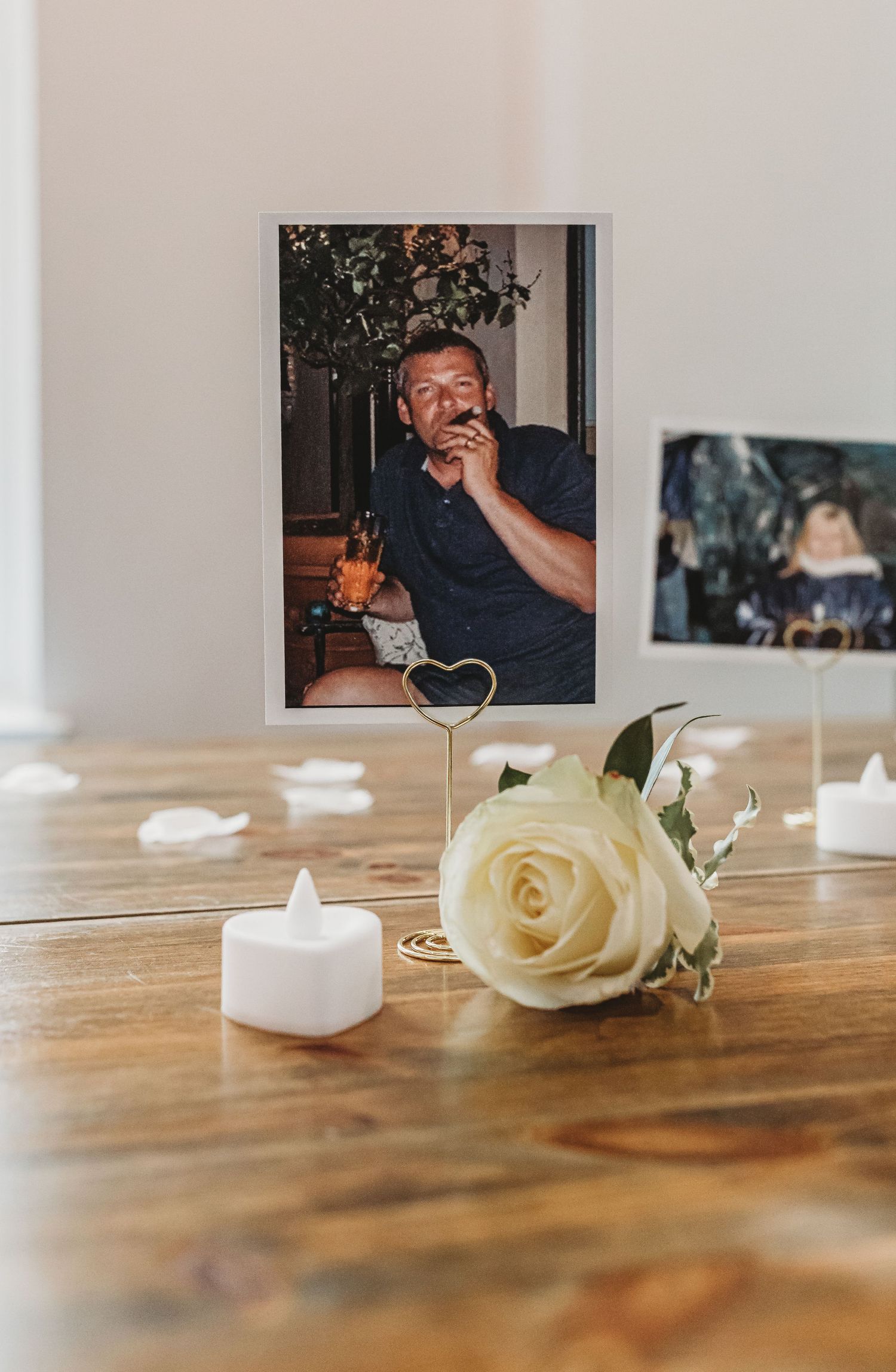Memorial photo display with white rose and tea lights on wooden table.