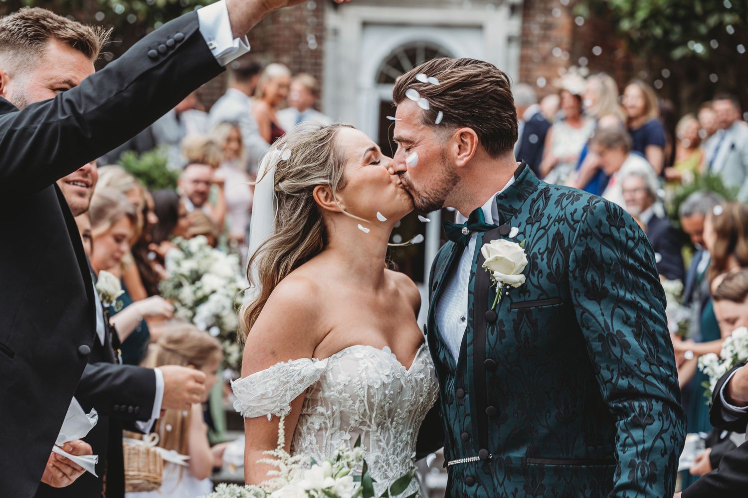 Newly married couple shares a joyful kiss during outdoor wedding ceremony while guests celebrate.