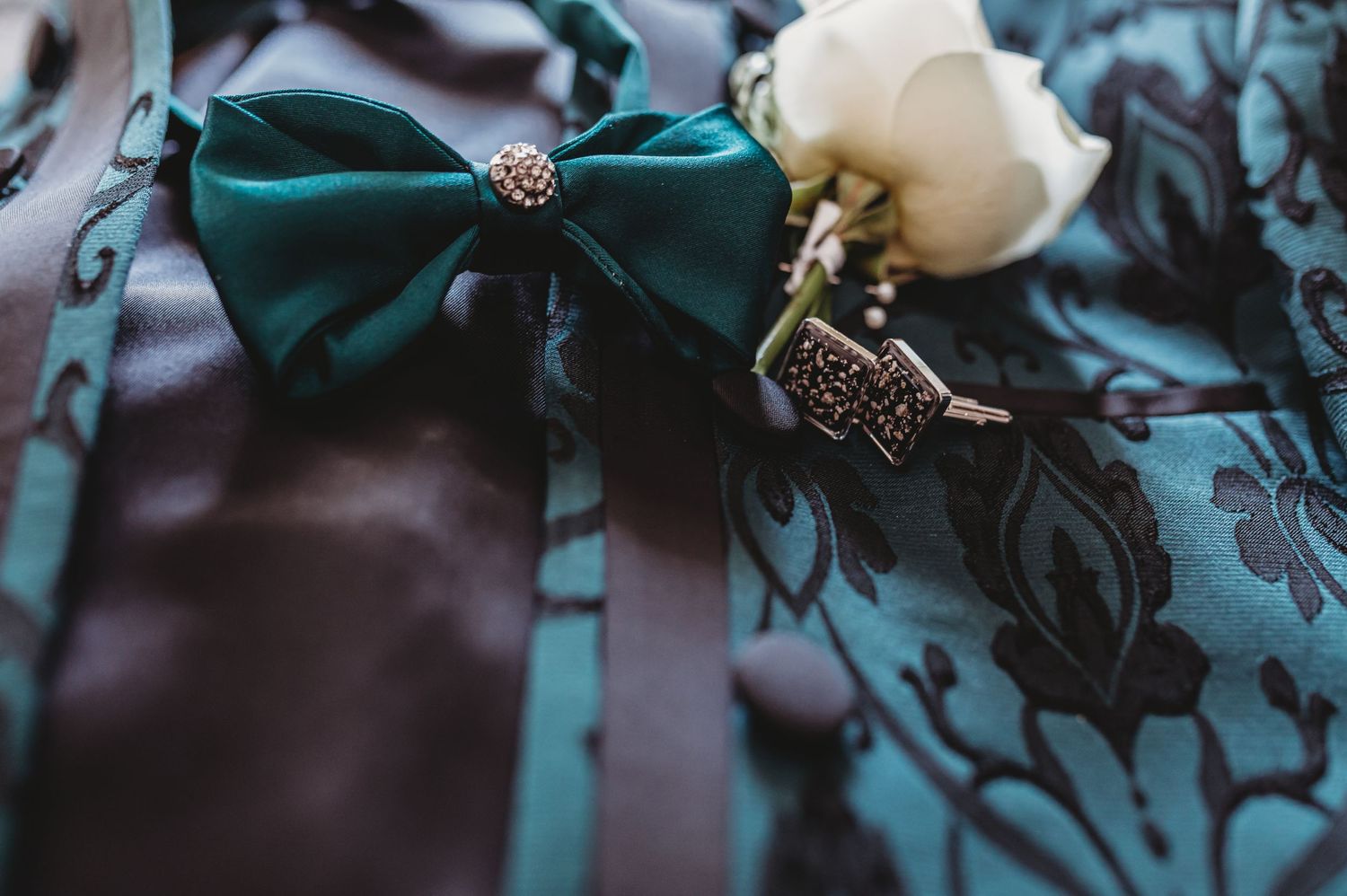 Emerald green bow tie and white rose boutonniere with decorative details.
