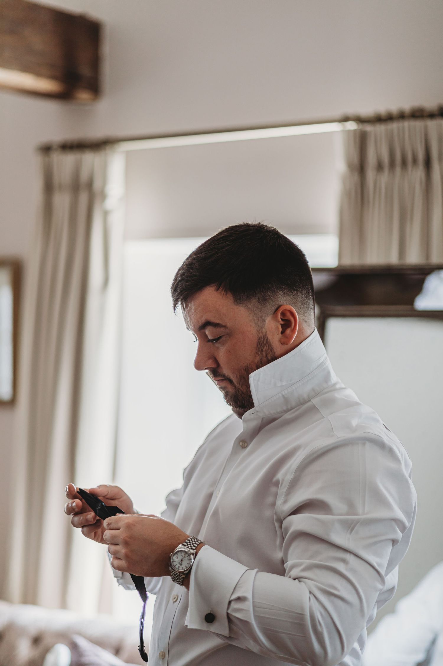 Side profile of someone in white formal attire checking their phone during wedding preparations.