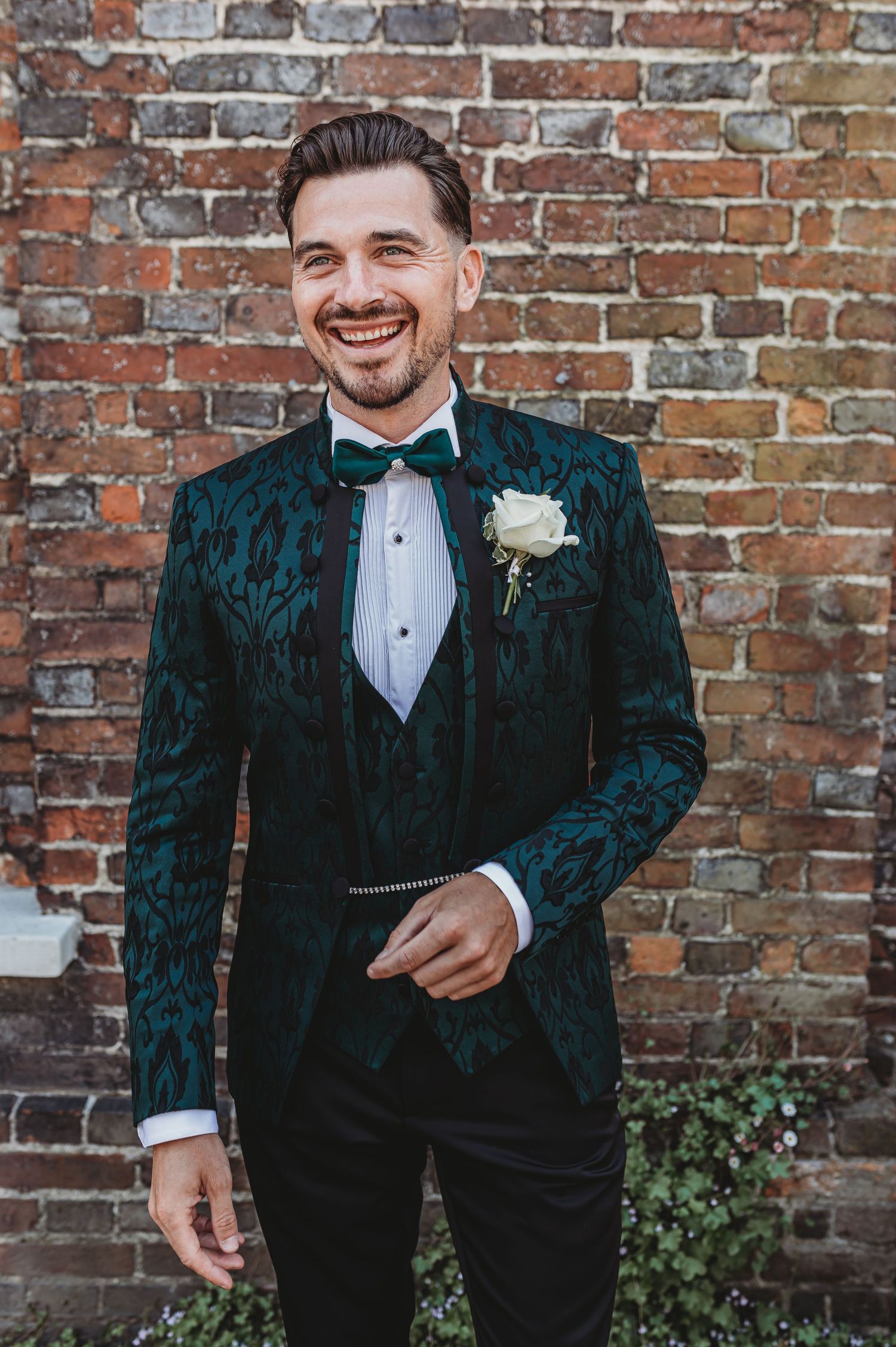 A joyful moment captured against brick wall wearing emerald velvet tuxedo with white boutonniere.