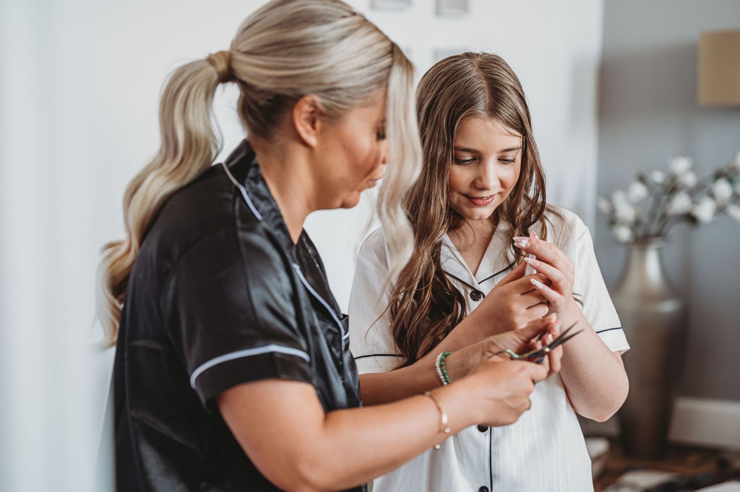 Two women examine and interact with a small object during wedding preparations.