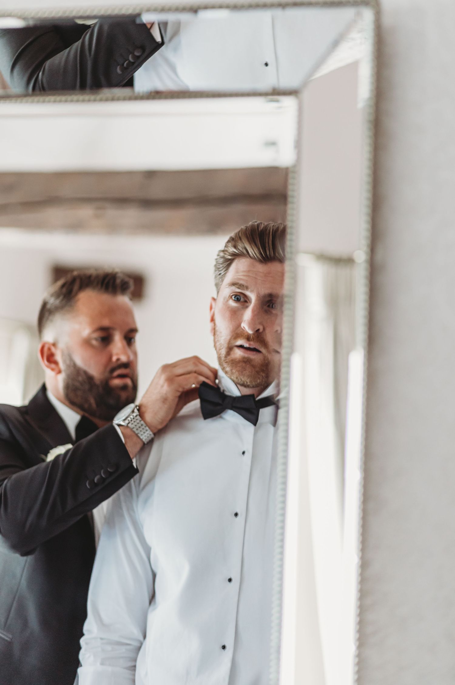 Wedding preparation captured in mirror reflection as formal attire is adjusted.
