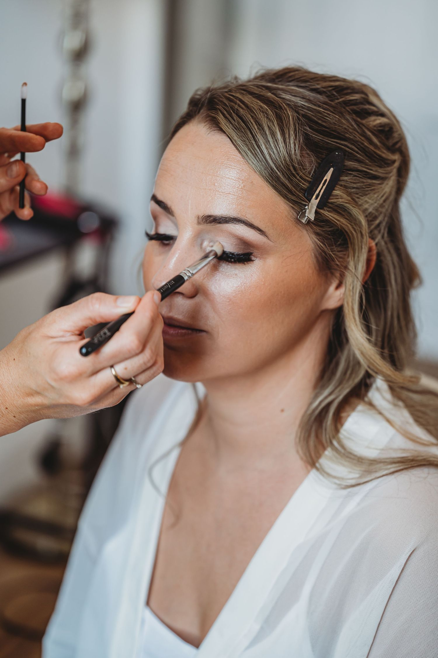 Professional makeup artist applying eyeshadow to a woman in a white robe during wedding preparations.